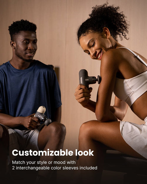 In a well-lit room, a man and a woman are using RENPHO US's Mini Thermal Massage Guns on their arms. The woman is dressed in a white sports outfit, while the man wears a navy blue sports shirt. Both look relaxed and focused as they enjoy their massages. At the bottom of the image, text reads: "Customizable look: Match your style or mood with 2 interchangeable color sleeves included.