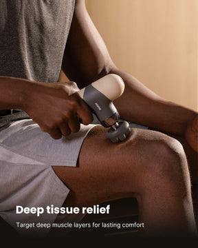 A person is uExperience on-the-go relaxation while also expressing your personal vibe with this pocket-sized massage solution that adds soothing warmth and style to your every day. (A)sing the RENPHO US Mini Thermal Massage Gun on their thigh for deep tissue relief. They are seated, wearing a gray pair of shorts. The background exudes soothing warmth, giving a relaxing ambiance. Text at the bottom reads, "Deep tissue relief - Target deep muscle layers for lasting comfort.