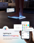 A person stands on the illuminated Elis Chroma Smart Scale by Renpho, displaying the time as 07:00. Beside it, a hand holds a smartphone showing the Renpho Health app with options to set reminders and choose themes. Text reads: "Lighting to Remind Weighing." The body fat scale automatically lights up at the specified time.