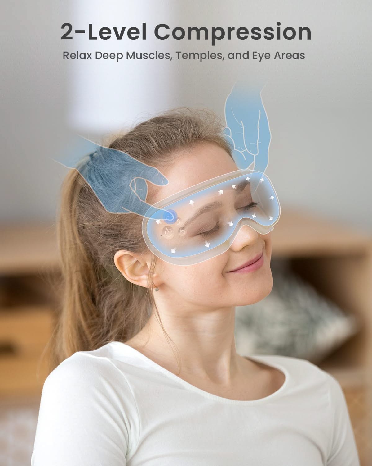 A woman with brown hair tied back is seated and wearing a white long-sleeved shirt. She has her eyes closed and is smiling while using the RENPHO US Eyeris 1 Eye Massager, which is light blue and has a Bluetooth feature. Illustrations show hands applying gentle pressure to the mask, stating, "2-Level Compression: Relax Deep Muscles, Temples, and Eye Areas." A blurred wooden furniture piece is in the background.