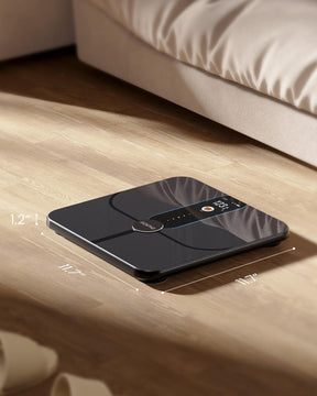 A modern Renpho Elis Nova Smart Scale displaying 1.24" on its screen, placed on a wooden floor next to a bed. (A)