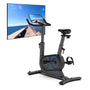 The Renpho AI Smart Bike S, featuring a sleek black design with blue accents, is placed in front of a wall-mounted TV. The screen displays a scenic coastal cycling route complete with ocean views, providing an immersive indoor cycling experience. A smaller digital screen on the bike's handlebars shows detailed cycling statistics to enhance your ride. (A)