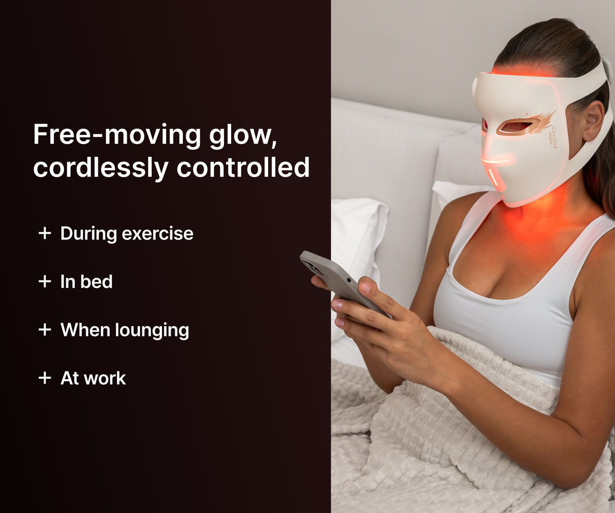 Woman in bed using her phone while wearing a cordless LED face mask, for use in bed, at work or during exercise